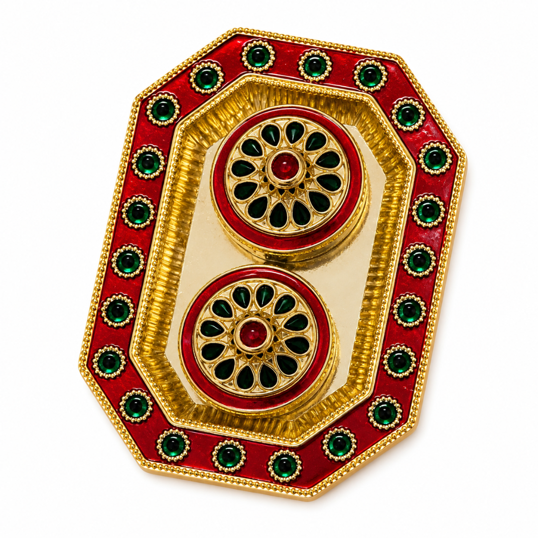 A decorative gold-plated brass tray with red enamel and green stone accents, featuring two circular motifs on a white background.