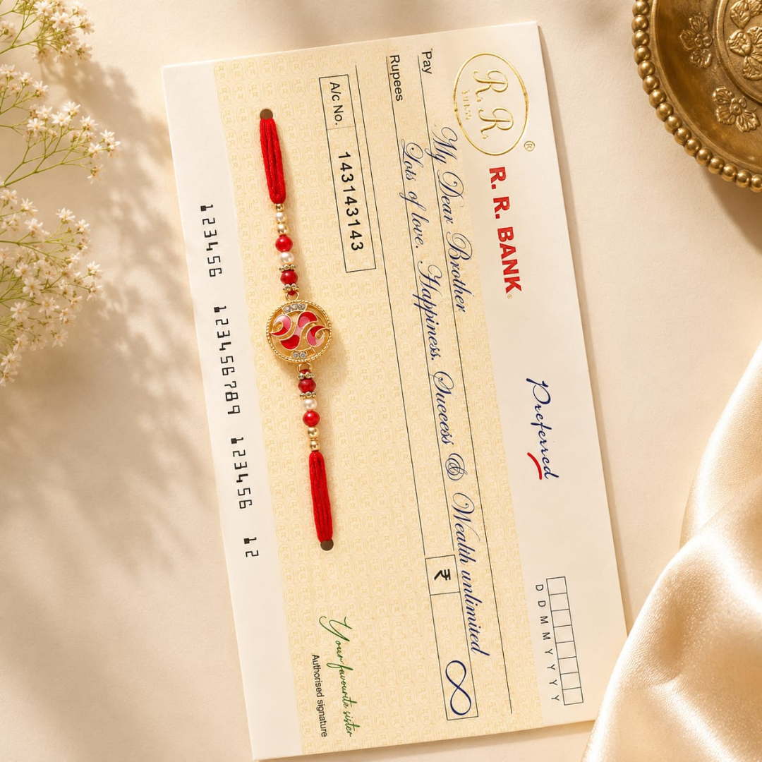 A traditional Indian Rakhi with red beads and a gold-toned circular pendant featuring a floral motif, laid flat on a cream-colored bank slip. The bank slip is styled on a beige surface with soft white flowers on the left and a gold decorative plate on the right.