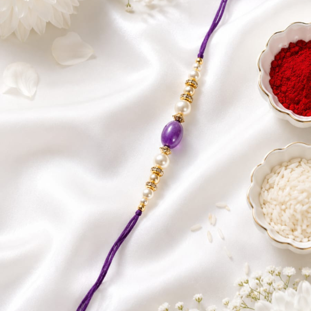 A purple and gold beaded Rakhi laid diagonally on white satin fabric, surrounded by decorative white flowers and small bowls of red powder and white rice.